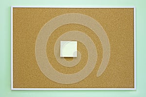 Brown cork message board with yellow stick note on the light green or blue wall