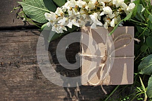 Brown craft gift box decorated with natural herbs and flowers on old wooden background with copy space. Floral decor elements. Fat