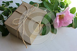 Brown craft gift box decorated with pink wild rose hips flower on old wooden background with copy space. Floral decor elements.