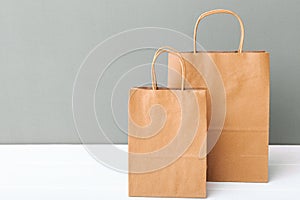Brown craft paper bags. Empty cardboard paper package. Shopping Mockup bags on white table gray background with copy space.