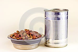 Brown crunchy organic kitty kibble pieces in a bowl and wet cat food in metal can for pet feed on light background.