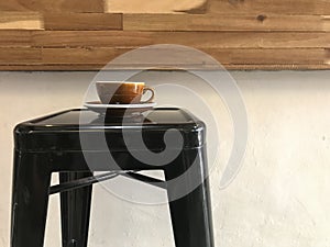 Brown cup of hot coffee with saucer on black metal bar stool