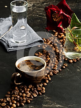 Brown cup with a strong freshly brewed espresso on a black background. Roasted coffee beans are located around the cup. Next to