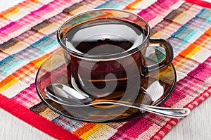 Brown cup with tea, spoon on saucer on checkered napkin