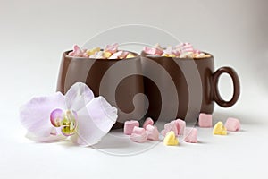 Brown cups of hot cocoa with marshmallows in heart shape on white background
