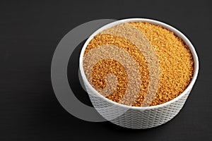 Brown Demerara Sugar in a Bowl on a black background, side view. Copy space
