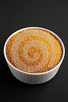 Brown Demerara Sugar in a Bowl on a black surface, side view