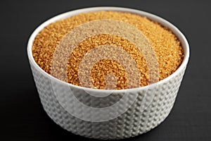 Brown Demerara Sugar in a Bowl on a black surface, side view