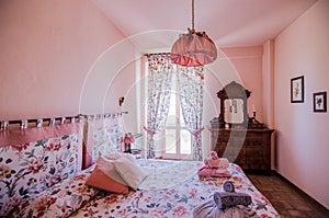 Brown dresser with mirror in pink room with curtained windows near flower patterned bed with pillows