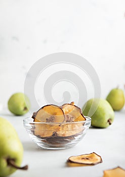 Brown dried pear chips slices in glass bowl with green pears on light table.Macro