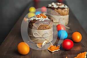 Brown Easter cakes decorated with chocolate, almond flakes and dried apricots among colored Easter eggs and tangerine zest on