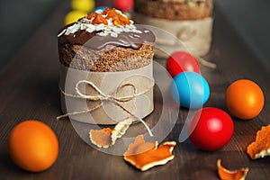 Brown Easter cakes decorated with chocolate, almond flakes and dried apricots among colored Easter eggs and tangerine zest on