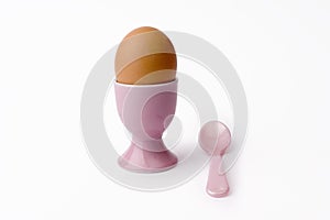 Brown egg in egg cup with spoon on white