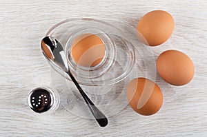 Brown egg on egg stand, spoon, boiled eggs, salt shakers on table. Top view