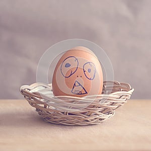 Brown egg with a face painted on it in a basket