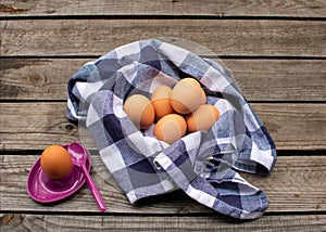 Brown eggs in a blue and white checked napkin, next to it an egg in a purple egg cup