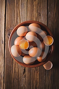 Brown eggs and broken eggs in a brown ceramic bowl on wooden table. Rustic Style. Eggs.