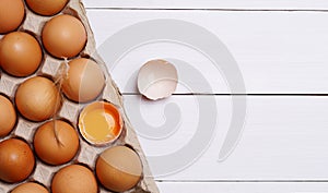 Brown eggs in carton box. Eggshell with egg yolk inside on white wooden background.