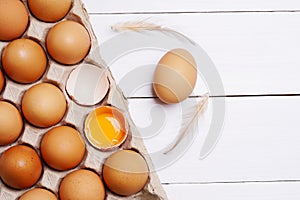 Brown eggs in carton box. Eggshell with egg yolk inside on white wooden background.