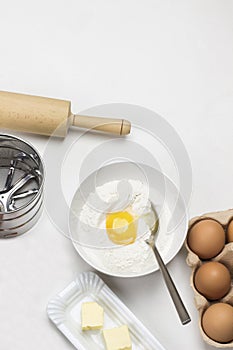 Brown eggs in carton container. Butter and whisk on plate. Egg yolk with flour in bowl