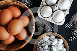 Brown eggs in a wooden bowl, white chicken eggs in a tray next to quail eggs and feathers