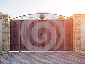 Brown expensive gate with forged pattern. Massive fence with iron brown sliding gates with wrought iron pattern. Sunset