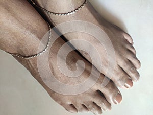 Brown feet with brown nail polish wearing silver anklet top angle