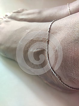 Brown feet with brown nail polish wearing silver anklet top angle