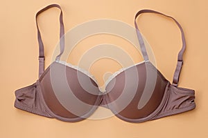 Brown female bra with smooth cups on a beige background.