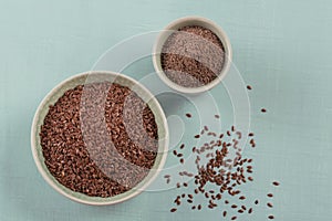 Brown flax seed and ground or crushed flaxseed or linseed in small bowl on a light blue background