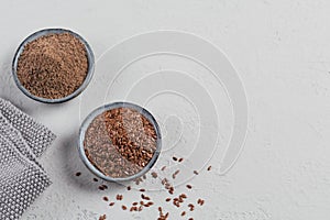 Brown flax seed and ground or crushed flaxseed or linseed in small bowl on light gray background