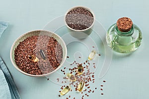 Brown flax seed or linseed and chia in small bowl and gelatin capsules with omega oil on a light blue background.