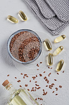 Brown flax seed or linseed in small bowl and gelatin capsules with linen seed oil on a light gray background.