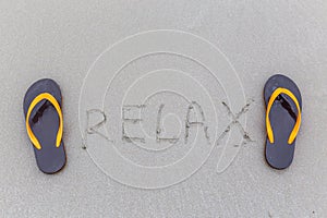 Brown flip-flops and relax word writing on sandy ocean beach, summer vacation concept.