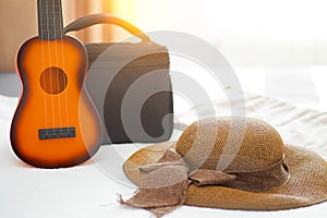 Brown floopy hat with ribbon, little guitar toy and suitcase background. Summer holiday concept