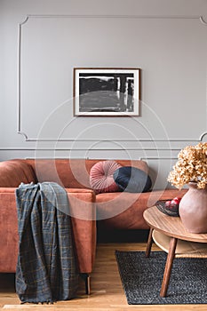 Brown flowers in pottery vase on stylish coffee table in chic living room interior with black and white poster on the grey wall