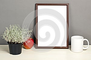 Brown frame mockup with plant pot, mug and apple on wooden shelf