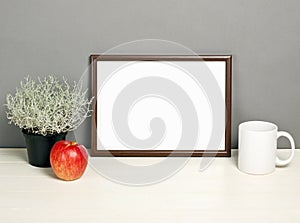 Brown frame mockup with plant pot, mug and apple on wooden shelf