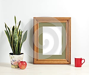 Brown frame mockup with plant pot, mug and apple on wooden shelf