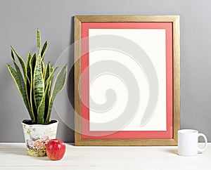 Brown frame mockup with plant pot, mug and apple on wooden shelf