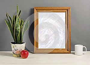 Brown frame mockup with plant pot, mug and apple on wooden shelf