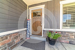 Brown front door with glass pane and Welcome sign against gray and stone wall