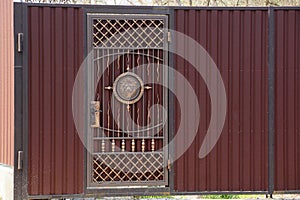 Brown gate and metal fence with forged pattern on the street