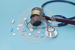 Brown gavel, medical stethoscope and scattered pills on a blue background.