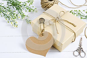 Brown gift box with heart tag label on wooden table with white daisy flower and vintage pin