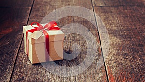 Brown gift box and red ribbon with tag on wood background with s