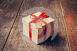 Brown gift box and red ribbon with tag on wood background with s