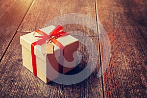 Brown gift box and red ribbon with tag on wood background with s