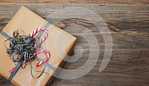 Brown gift box with ribbon and candy cane on wooden background.