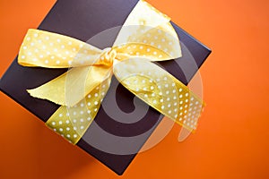Brown gift box with yellow ribbon on orange background. Top view with copy space.
